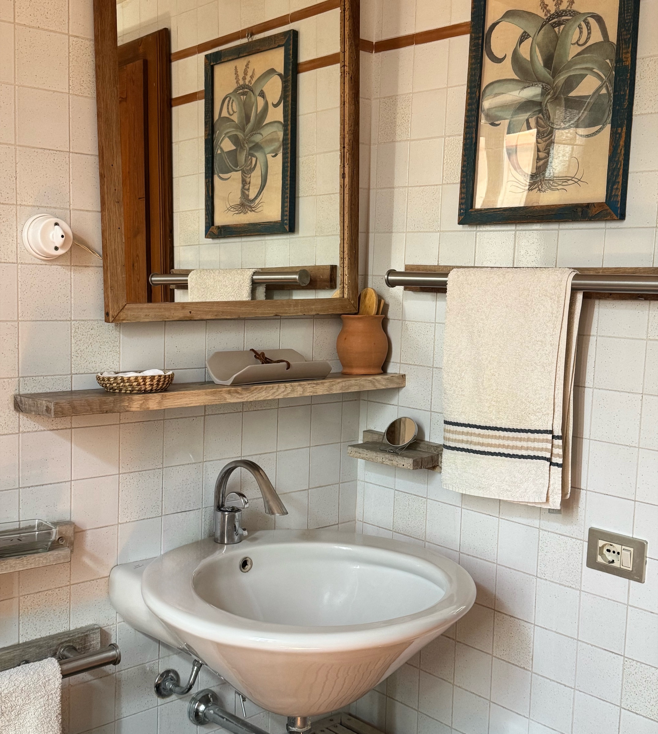 Il lavabo con lo specchio, le stampe botaniche e le piastrelle bianche