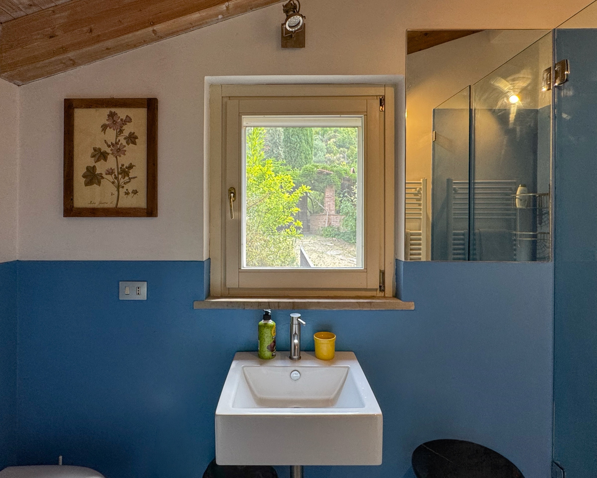 Il lavabo sotto la finestra, fra la parete blu e il box doccia