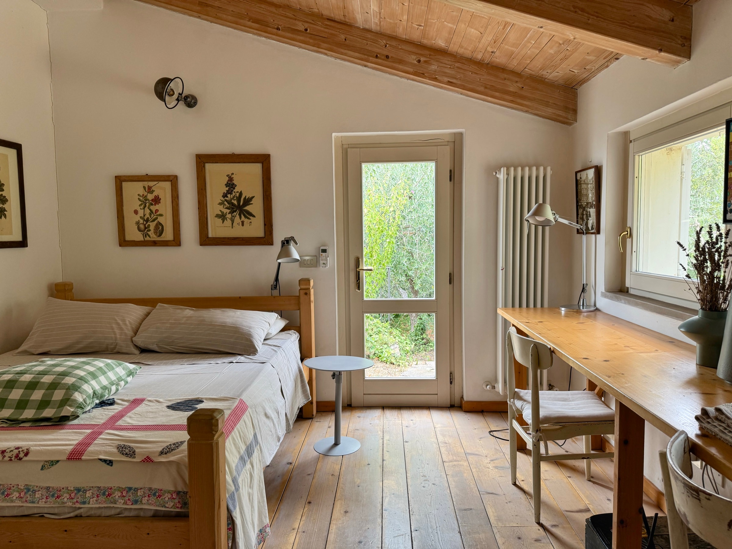 Il letto sotto le travi, la porta-finestra sul verde e la scrivania in legno