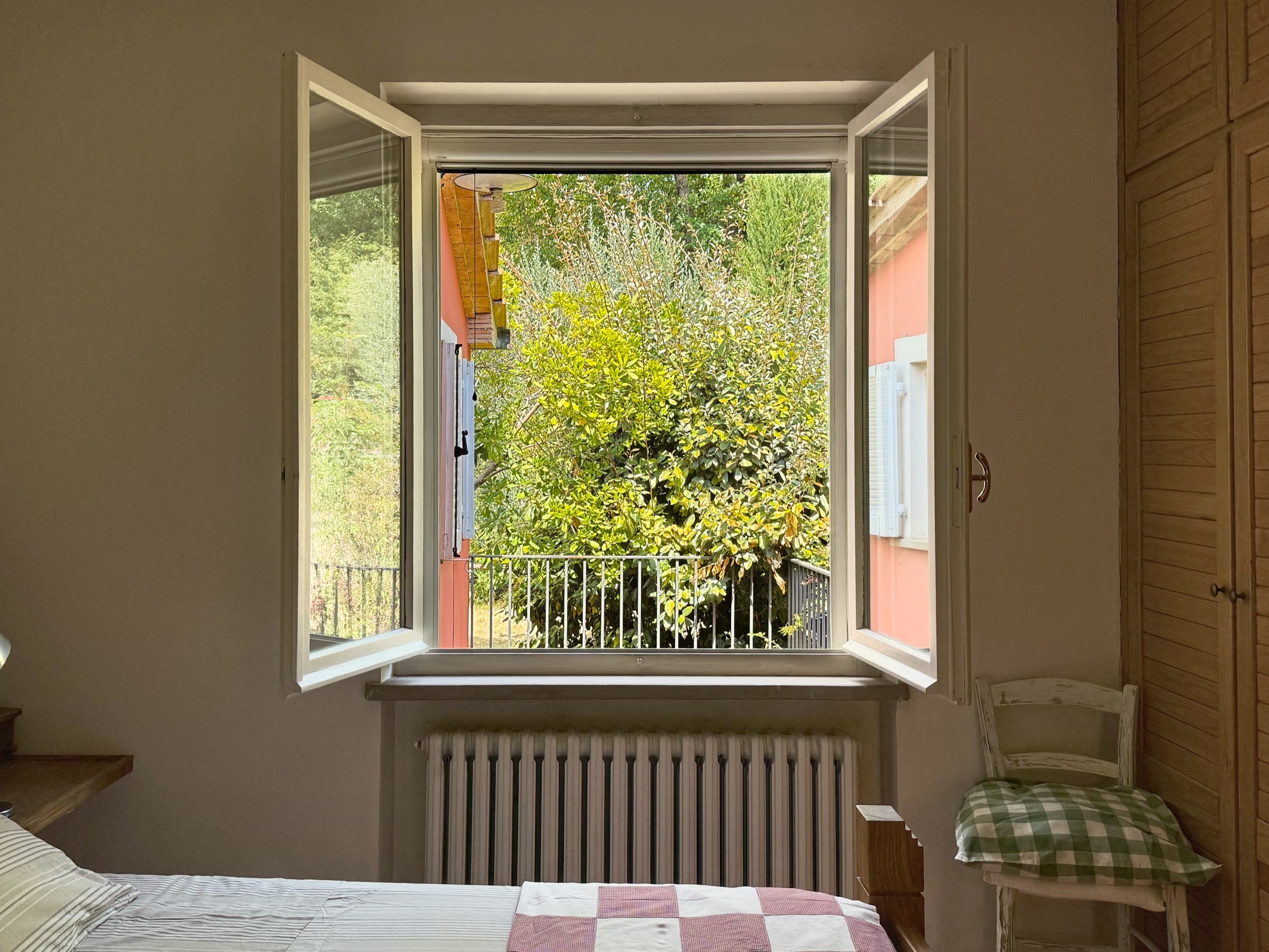 La finestra della camera matrimoniale, spalancata sugli alberi del giardino